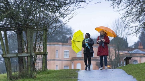 Two visitors with colourful umbrellas brave the wet weather to walk along the pathways around the grounds at Killerton, Devon